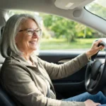 A cheerful senior woman sitting in the driver's seat of her car.