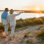 A senior couple walks along a sunny coastal trail at sunset, representing a healthy and active retirement lifestyle in a warm climate.